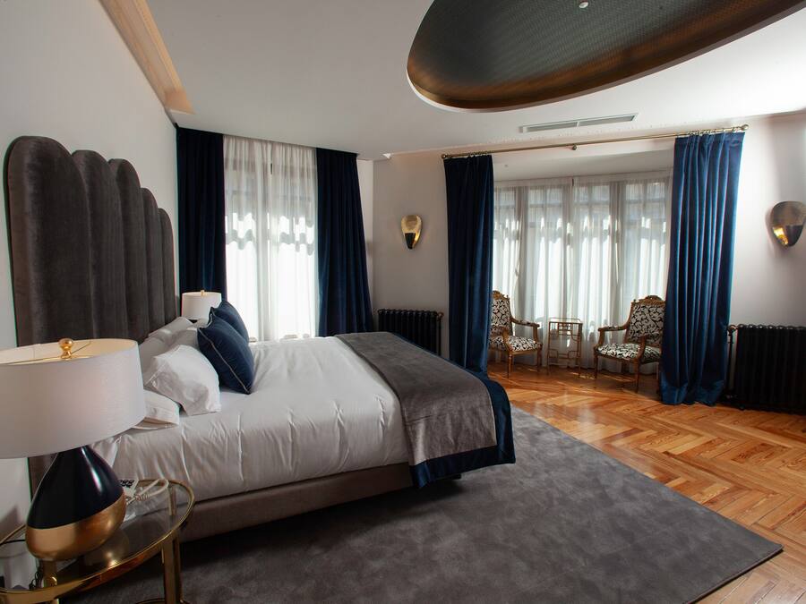 Habitación de hotel moderna con una cama grande, un área de descanso con dos sillones y vistas al exterior a través de amplios ventanales.