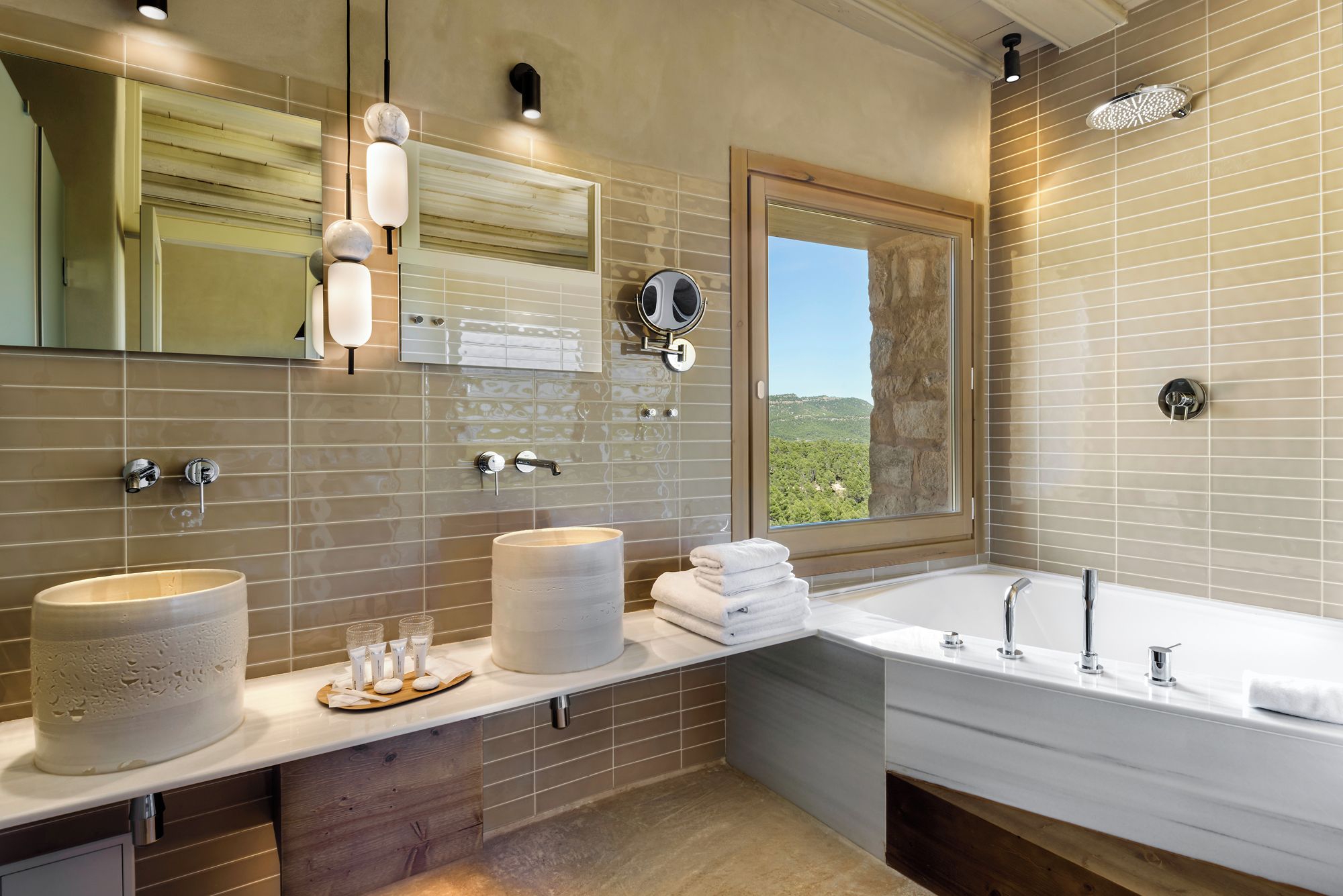 Une salle de bain moderne avec un grand miroir, deux lavabos, une baignoire et une fenêtre donnant sur un beau paysage.