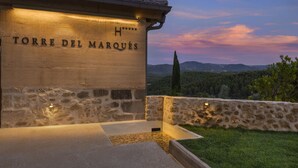 A stone building with "TORRE DEL MARQUES" engraved on its facade, set against a backdrop of a twilight sky and distant mountains. - Torre del Marqués Hotel Spa & Winery - Small Luxury Hotels (Monroyo)