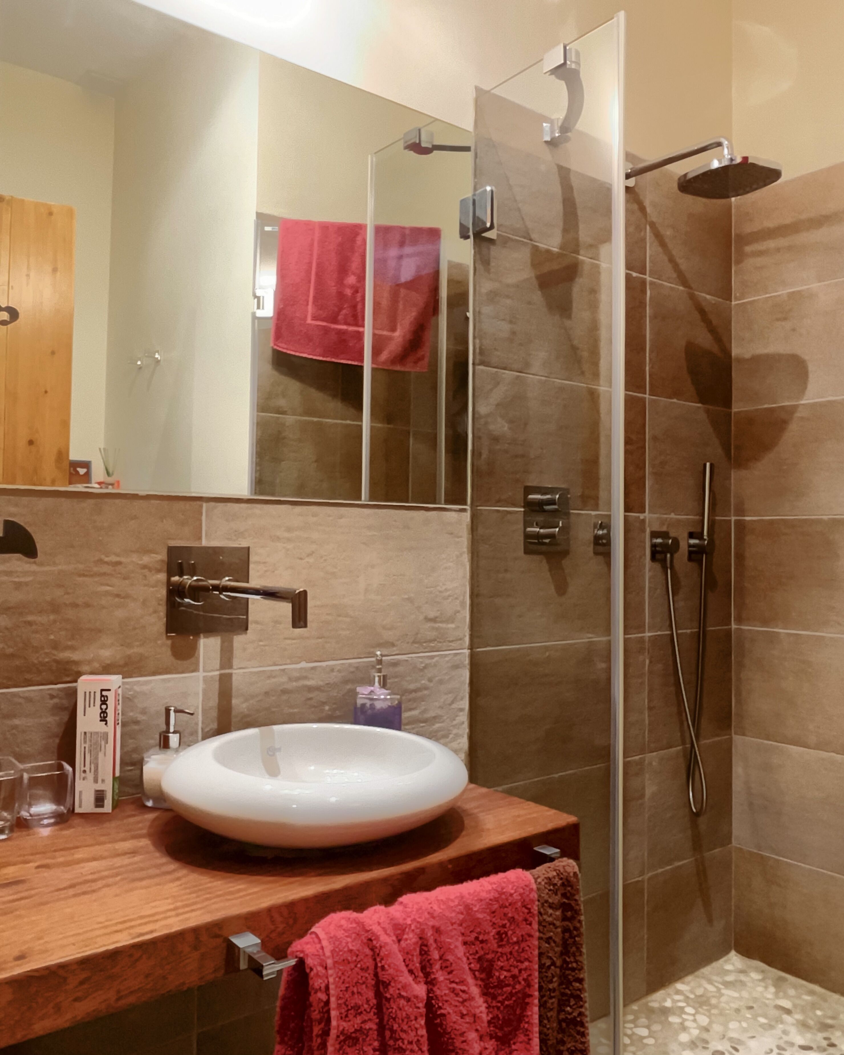 A bathroom with a wooden vanity, a white sink, a glass shower enclosure, and a red towel.