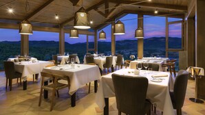 A restaurant with multiple tables and chairs, large windows with a mountain view, and hanging pendant lights. - Torre del Marqués Hotel Spa & Winery - Small Luxury Hotels (Monroyo)