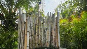 A traditional bamboo gate with a stone base, surrounded by lush greenery and palm trees.