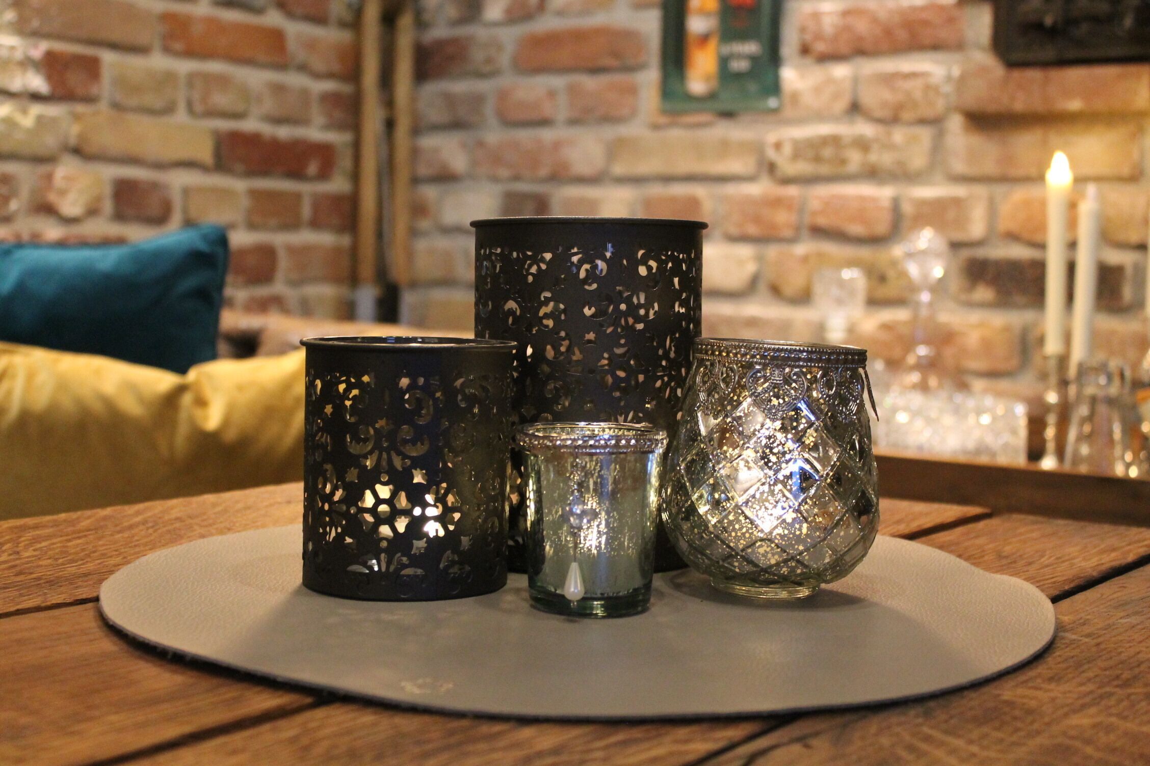 A table with three candle holders and a candle on a round mat.
