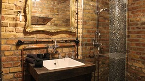 A bathroom with a rustic brick wall, a wooden vanity with a sink, a mirror with an ornate frame, and a shower with a glass enclosure. - Friendly Home - Special apartment "Old Bakery" (Dersdorf)