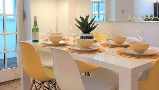 A dining area with a white table set for four, yellow chairs, and a large mirror above the table. - Seaside Cottage With Parking (Worthing)