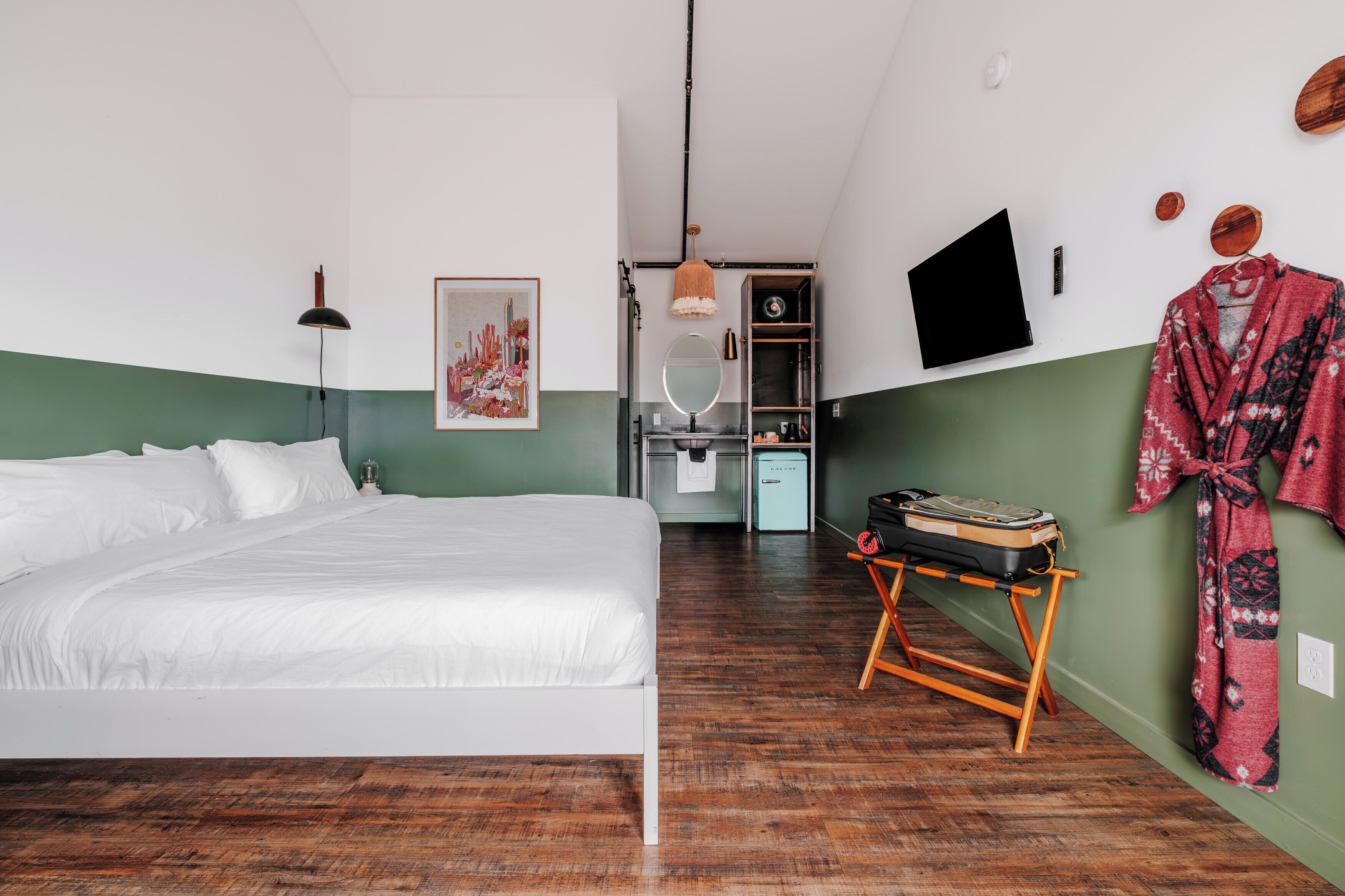 Un dormitorio con cama, escritorio y silla, espejo, armario y televisor en la pared.