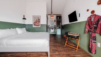 Un dormitorio con cama, escritorio y silla, espejo, armario y televisor en la pared.