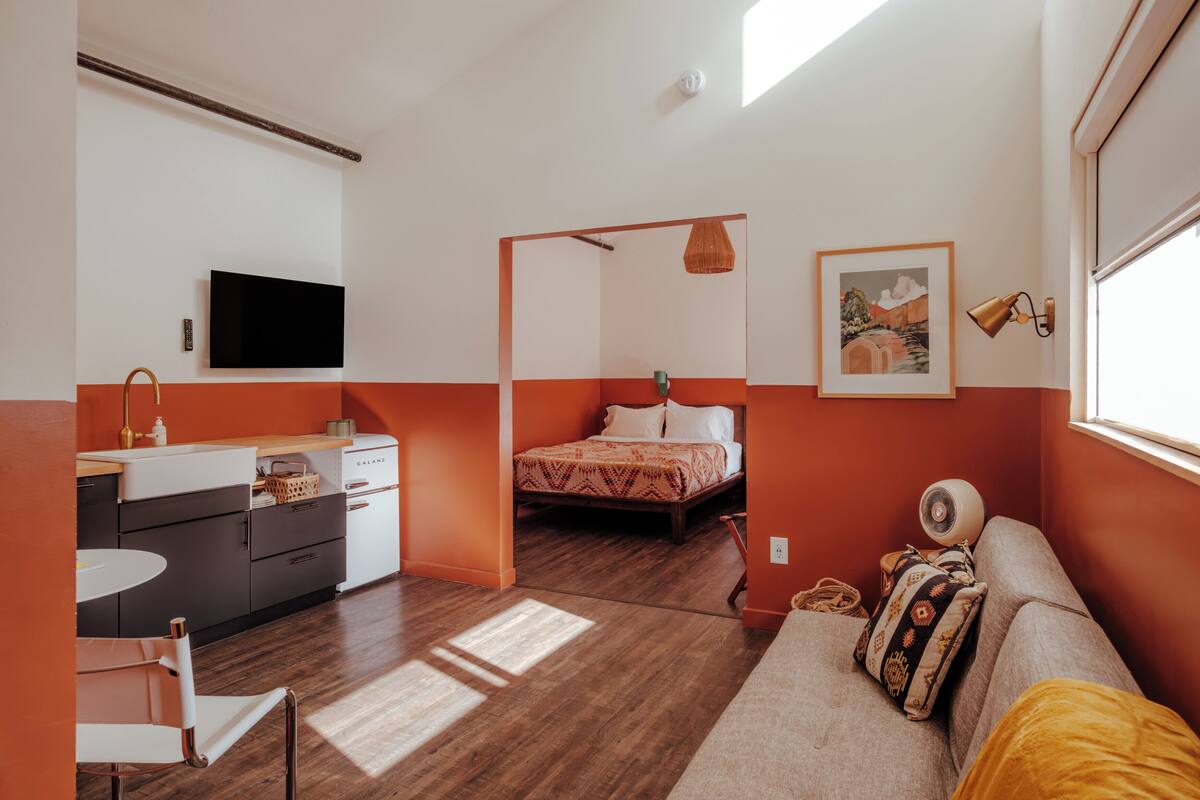 A compact room with a bed, a sofa, a TV, a kitchen area, and a window.