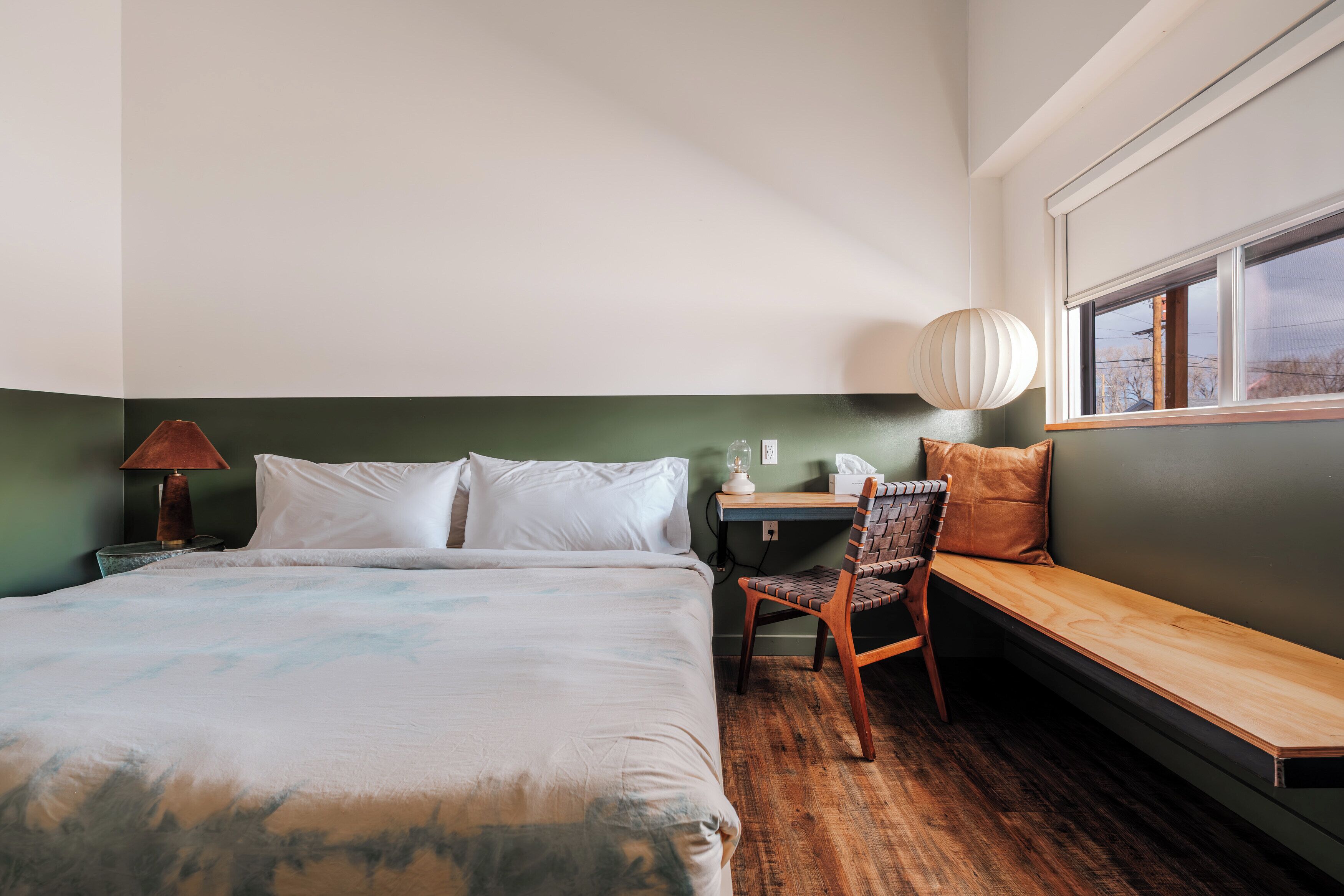 A bedroom with a bed, a desk, a chair, a lamp, and a window.