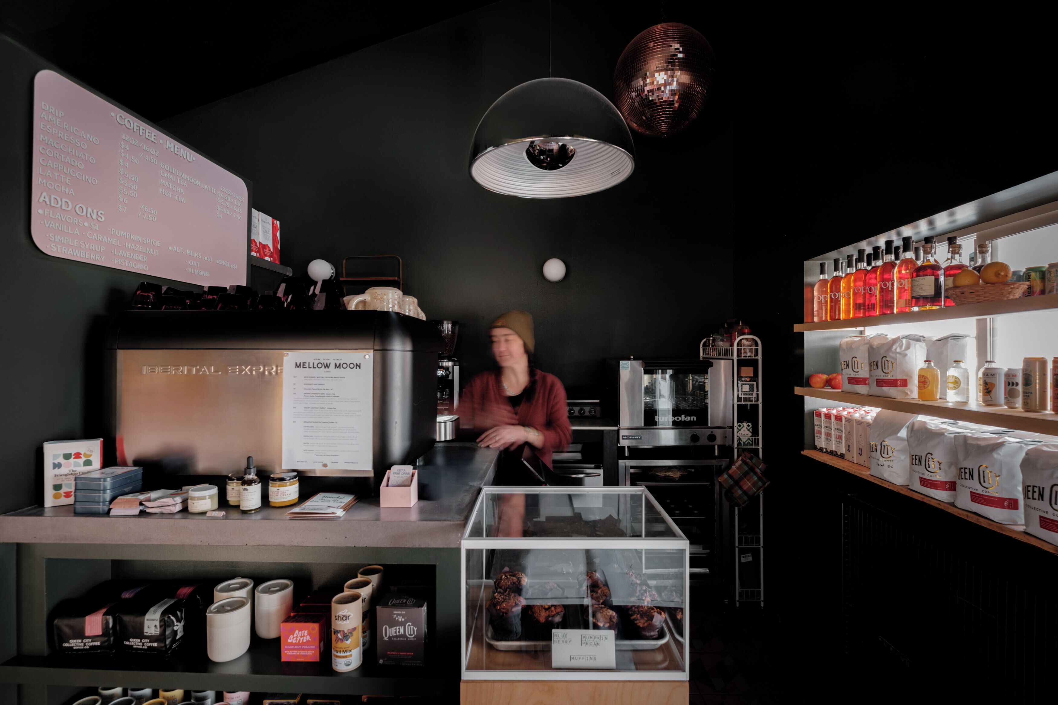 A coffee shop interior with a menu board, coffee machines, and shelves stocked with products.