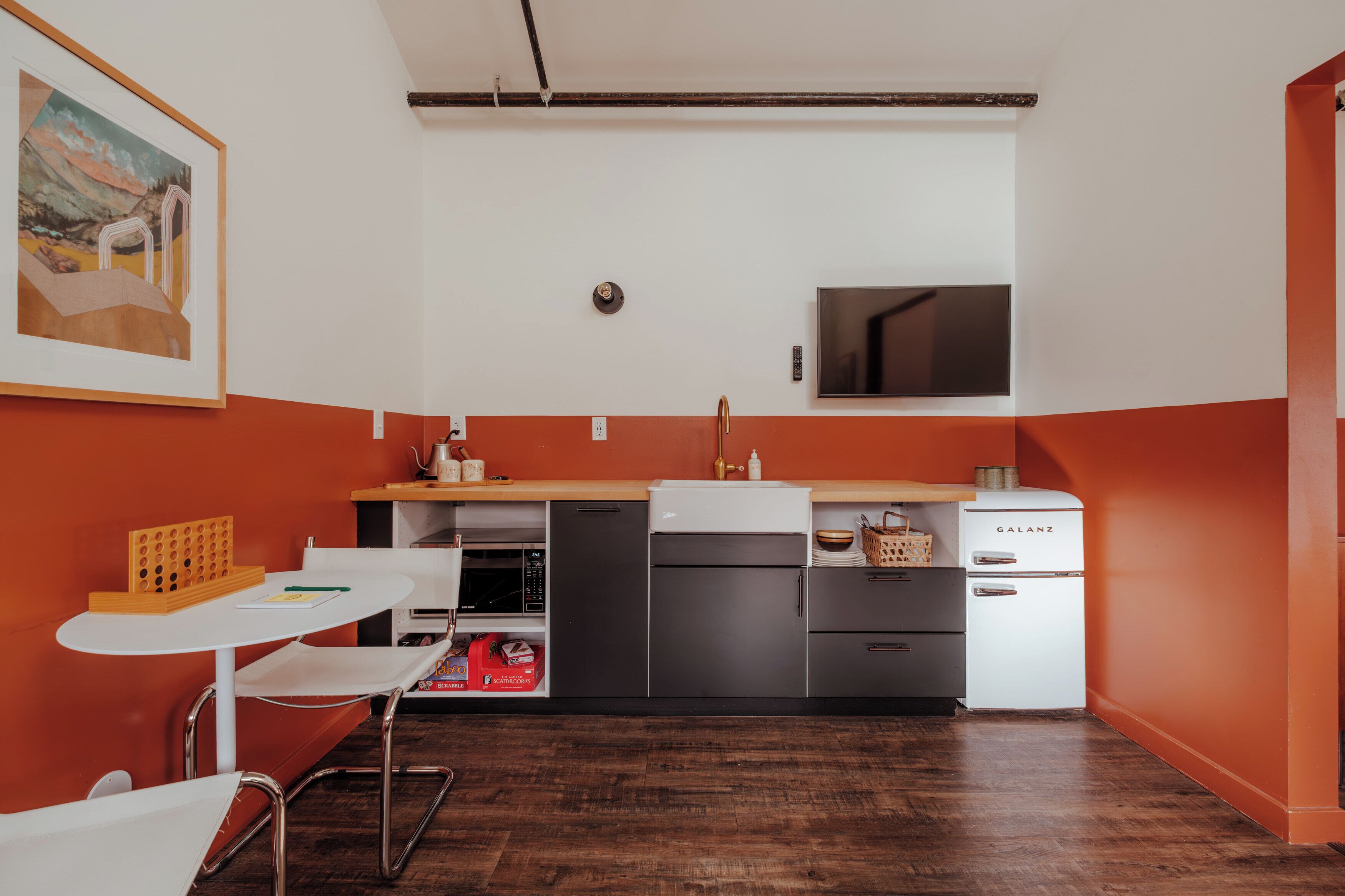 Cocina compacta con una decoración en blanco y naranja, microondas, lavabo y refrigerador Galanz.