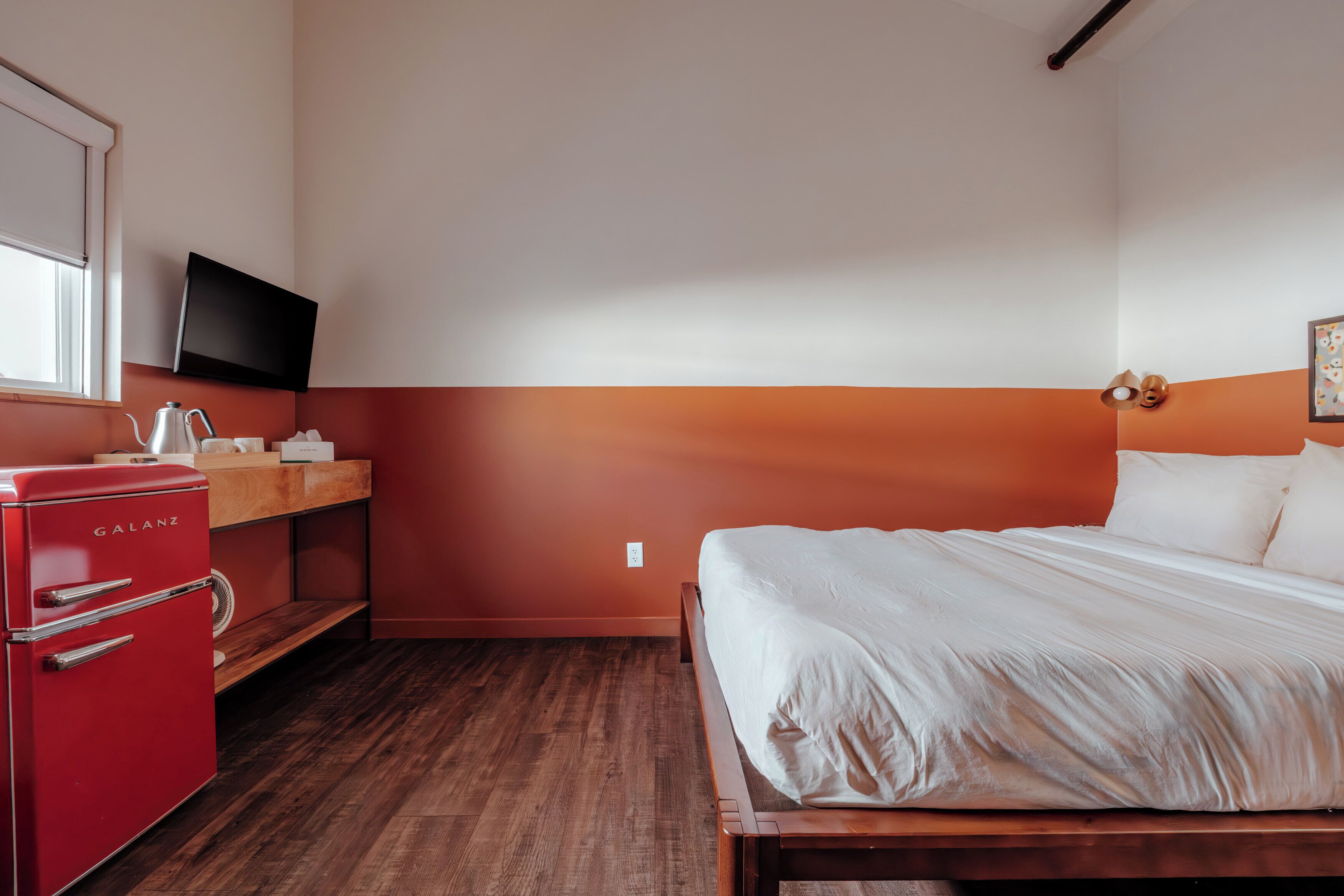 Una habitación de hotel con una cama, un electrodoméstico rojo, un televisor y una ventana.
