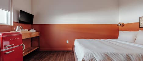 Una habitación de hotel con una cama, un electrodoméstico rojo, un televisor y una ventana.
