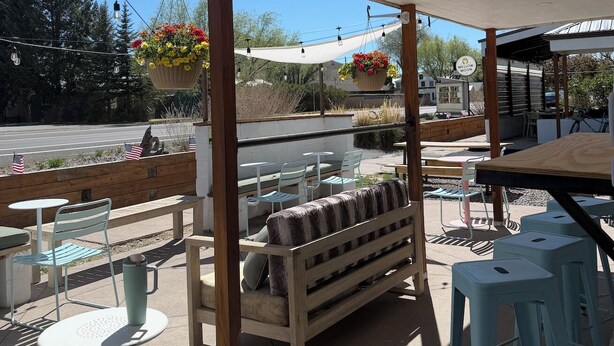 An outdoor patio with tables and chairs, hanging flower baskets, and a view of the street. - Mellow Moon Lodge (Del Norte)