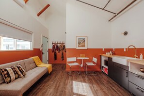 Un espace de vie compact comprenant un canapé, deux fauteuils, une petite table à manger et un coin cuisine.