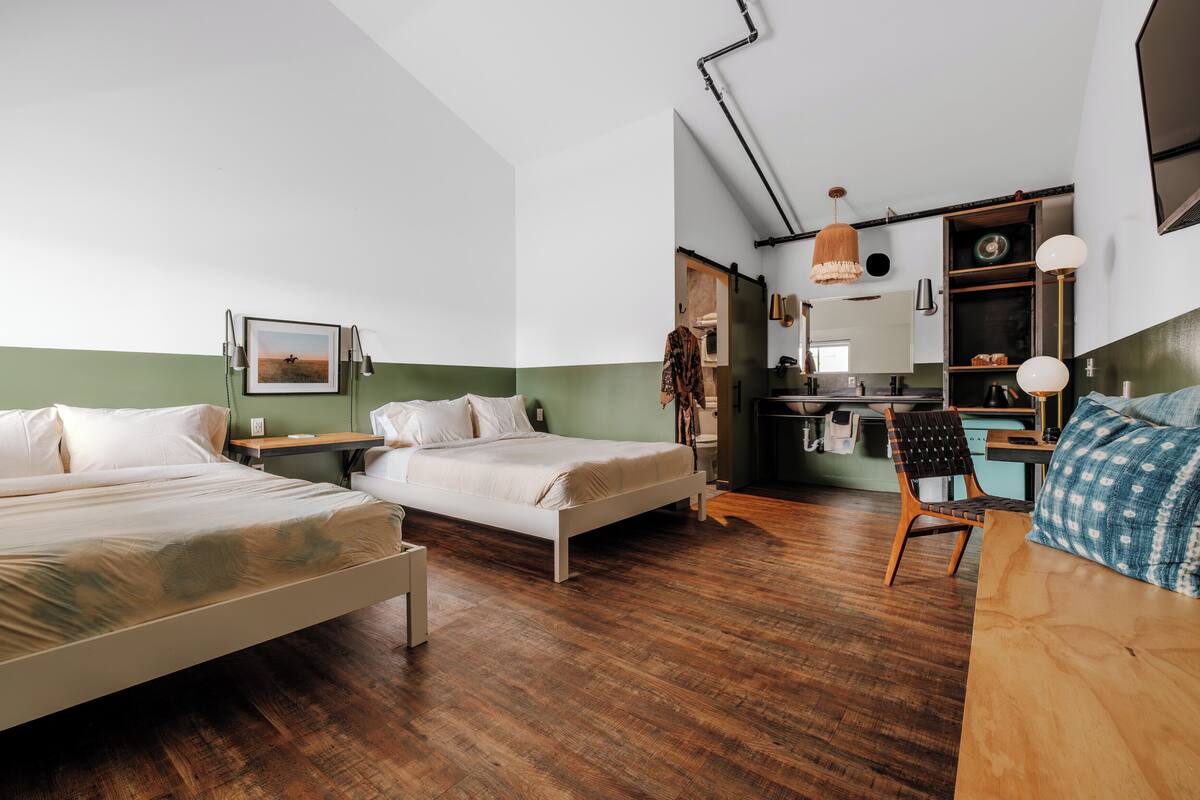 A room with two beds, a desk, and a kitchenette.