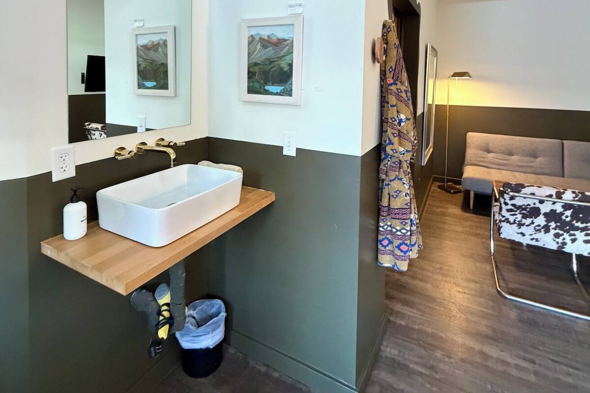 A modern bathroom with a large mirror, a white sink, and a wooden vanity.
