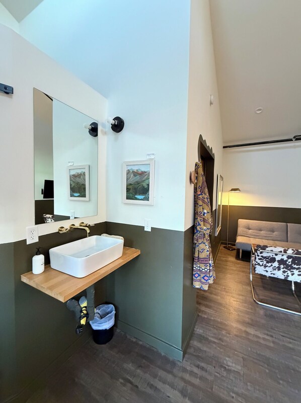 A modern bathroom with a large mirror, a white sink, and a wooden vanity.