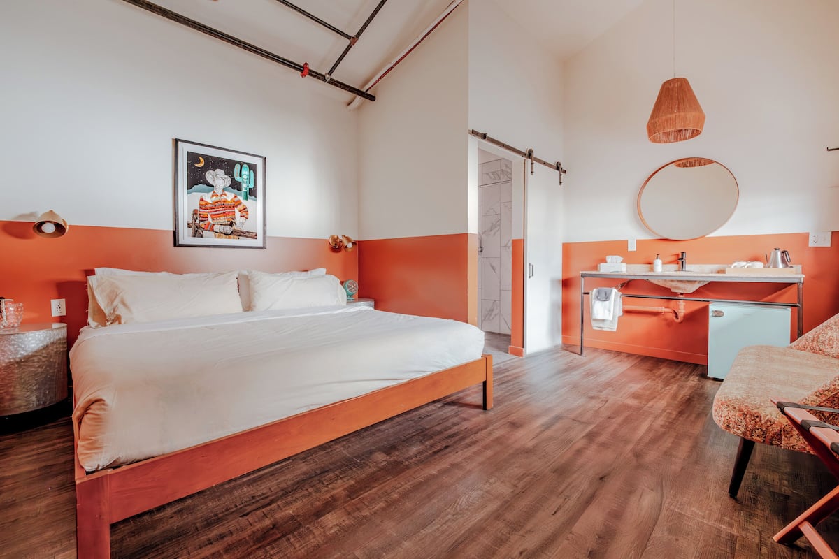 A modern bedroom with a wooden bed, a desk, a chair, a round mirror, and a framed picture on the wall.