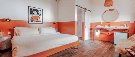 A modern bedroom with a wooden bed, a desk, a chair, a round mirror, and a framed picture on the wall.