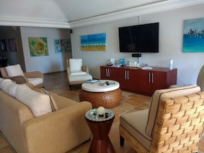 Uma sala de estar com sofá, poltronas, mesa de centro, televisão e armário.
