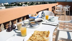A breakfast setup on a terrace with a table set for two, including plates of flatbread, bowls of jam, and a glass of orange juice. - Dar Iziki (Sidi Kaouki)