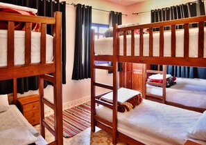 A bunk bed room with wooden frames, a small wooden dresser, and a patterned rug. - Dar Iziki (Sidi Kaouki)