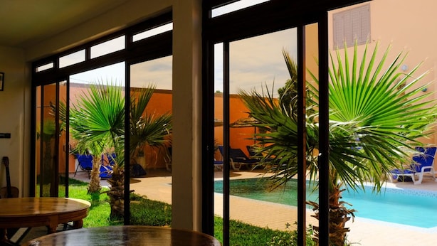 A poolside area with palm trees, a pool, and lounge chairs. - Dar Iziki (Sidi Kaouki)
