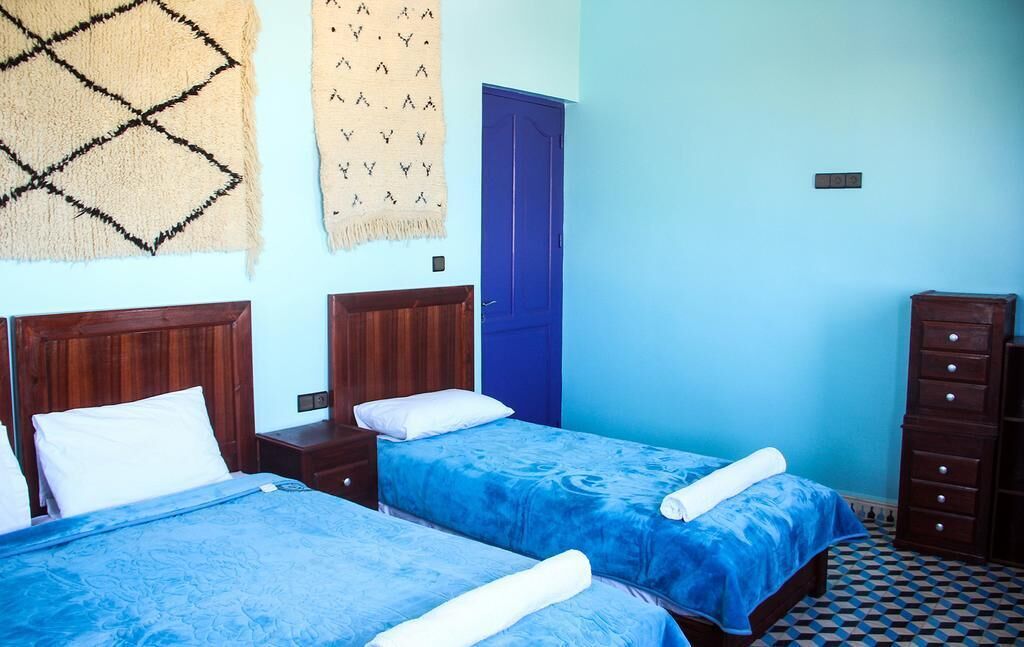 Ein Zimmer mit zwei Betten, einer blauen Tür und einem Teppich mit Muster.