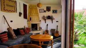 A cozy living room with a fireplace, a sofa, a coffee table, and musical instruments. - Dar Iziki (Sidi Kaouki)