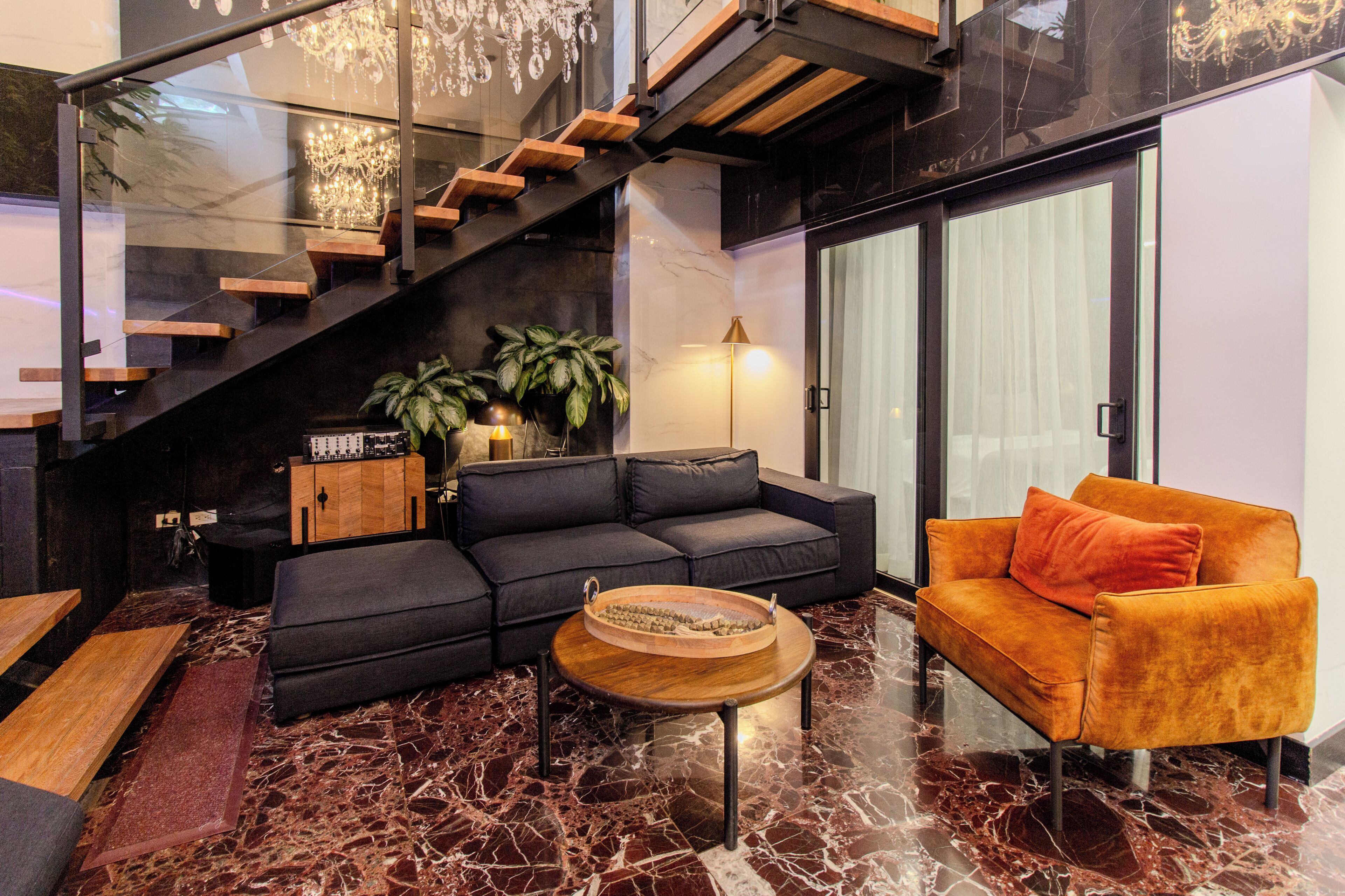 A modern living room with a black sectional sofa, an orange armchair, a wooden coffee table, and a staircase with wooden steps.
