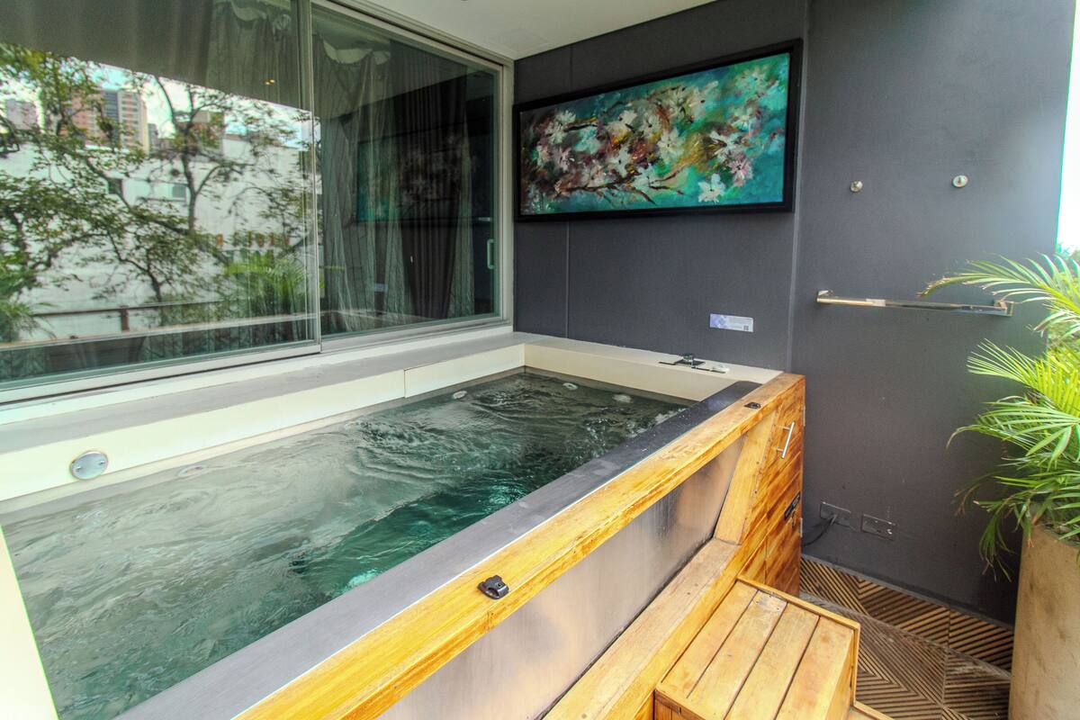 Un área de spa moderna con hidromasaje, asientos de madera y un amplio ventanal con vistas a la ciudad.