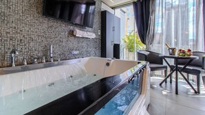 A modern bathroom with a large bathtub, a flat-screen TV mounted on the wall, and a small table with fruit. - Haven, A Design Hotel (Medellín)