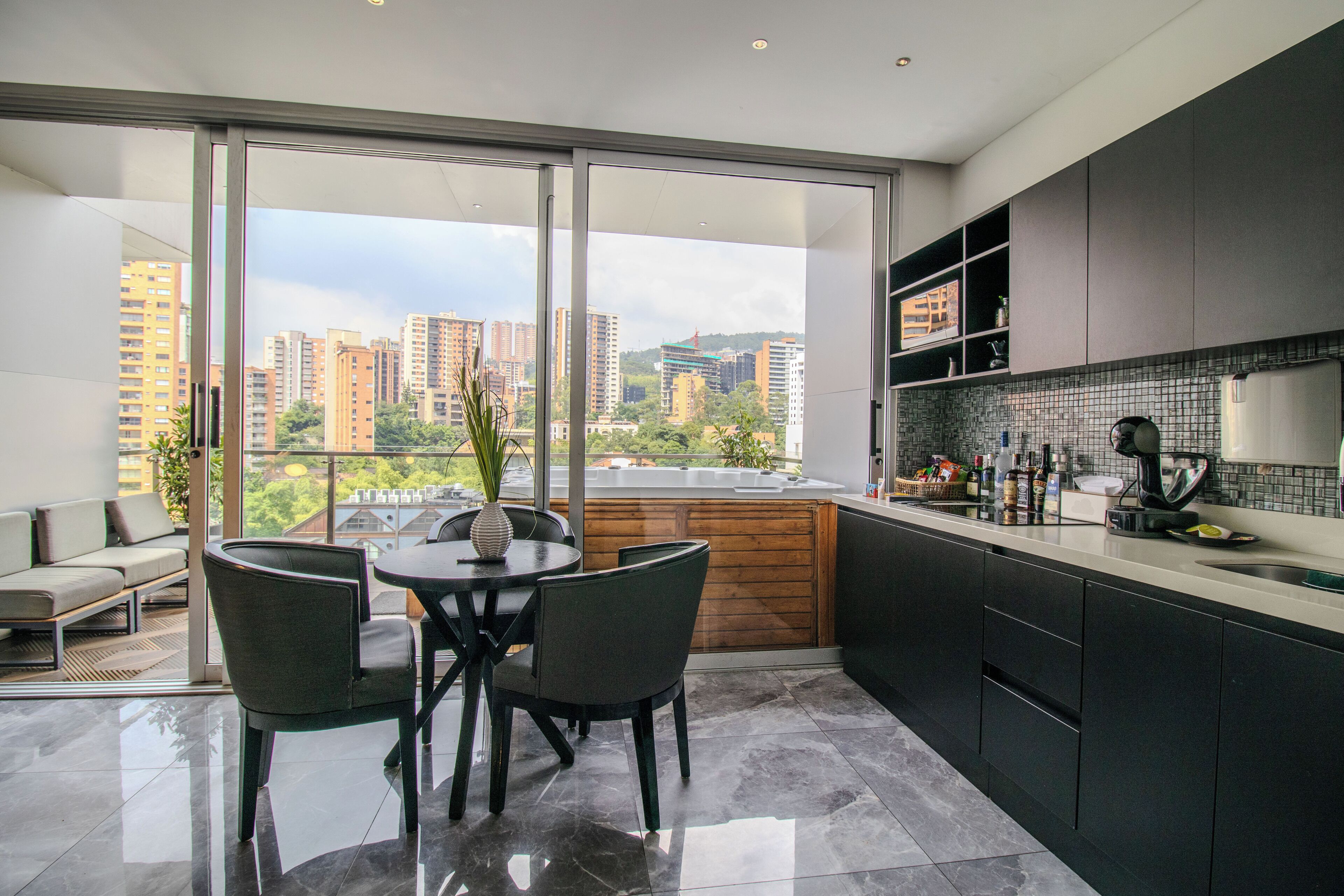 Una cocina moderna con un ventanal grande, un comedor con mesa y sillas, y vistas a rascacielos.