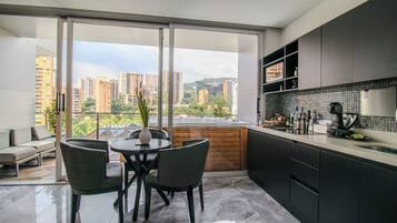 Una cocina moderna con un ventanal grande, un comedor con mesa y sillas, y vistas a rascacielos.