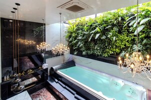 Un baño lujoso con piso de mármol, una bañera grande y una pared cubierta de vegetación.