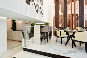 Um interior moderno com piso de mármore, uma área de recepção e um espaço de estar com mesas e cadeiras.