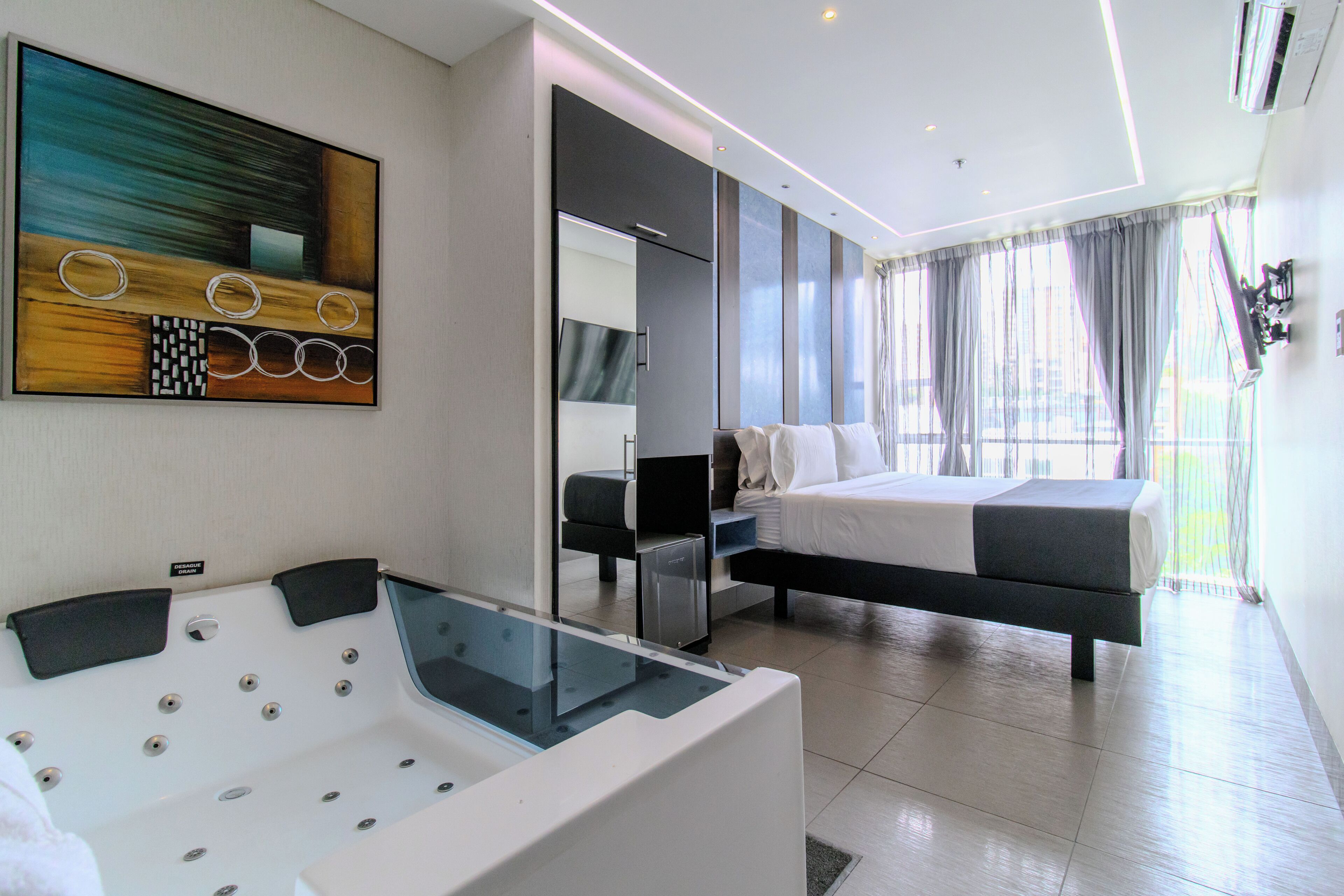 Ein modernes Hotelzimmer mit einem großen Bett, einer Glaskeramik-Badewanne und einem großen abstrakten Gemälde an der Wand.