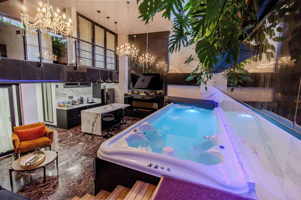 Un moderno espacio de spa con un jacuzzi, suelo de mármol, un sofá y una araña.