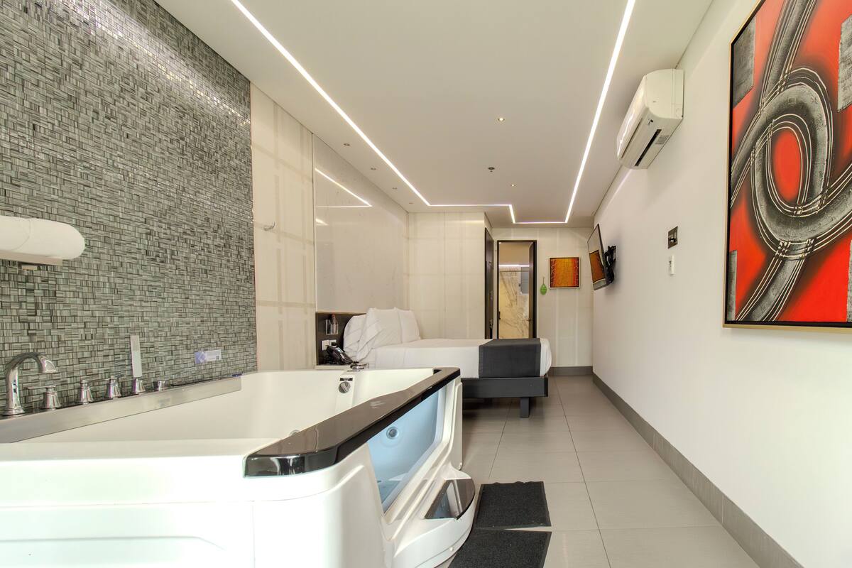 Un baño moderno con una bañera grande, una ducha y un inodoro. En la habitación contigua hay una cama y un escritorio.