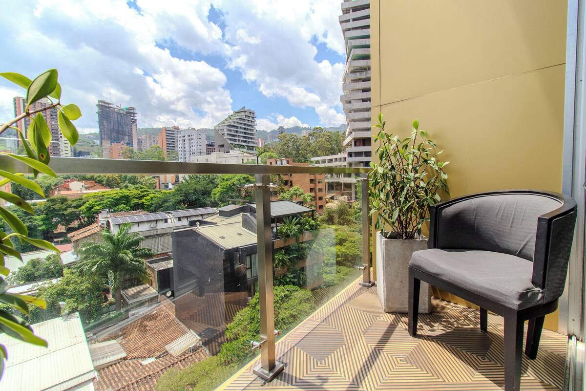 Un balcón con vistas a edificios circundantes, una silla y una planta en maceta.