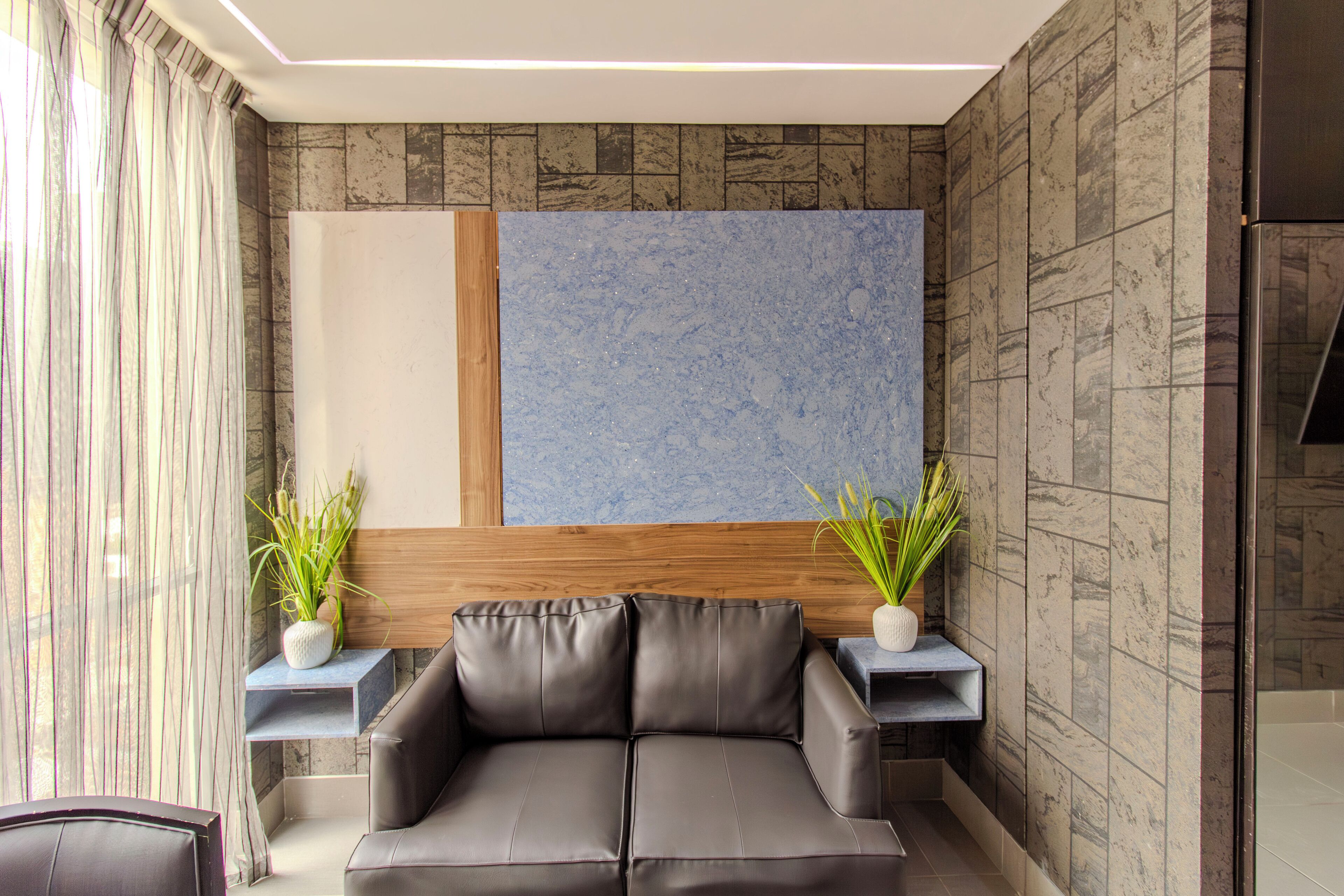 A modern living room with a leather sofa, two side tables with potted plants, a large abstract painting on the wall, and a wooden headboard.