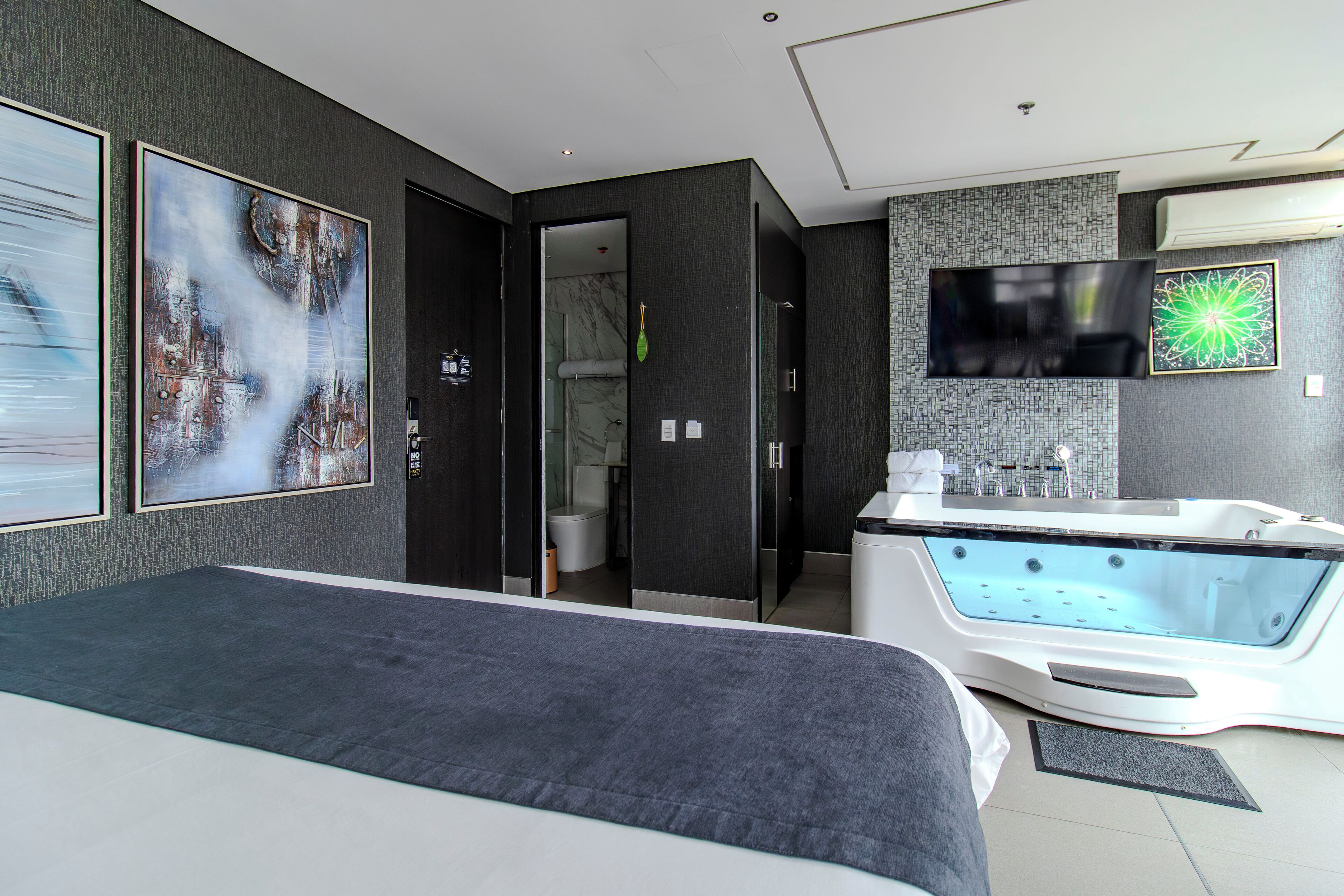 A modern hotel room with a large bed, a bathtub, and a TV mounted on the wall.