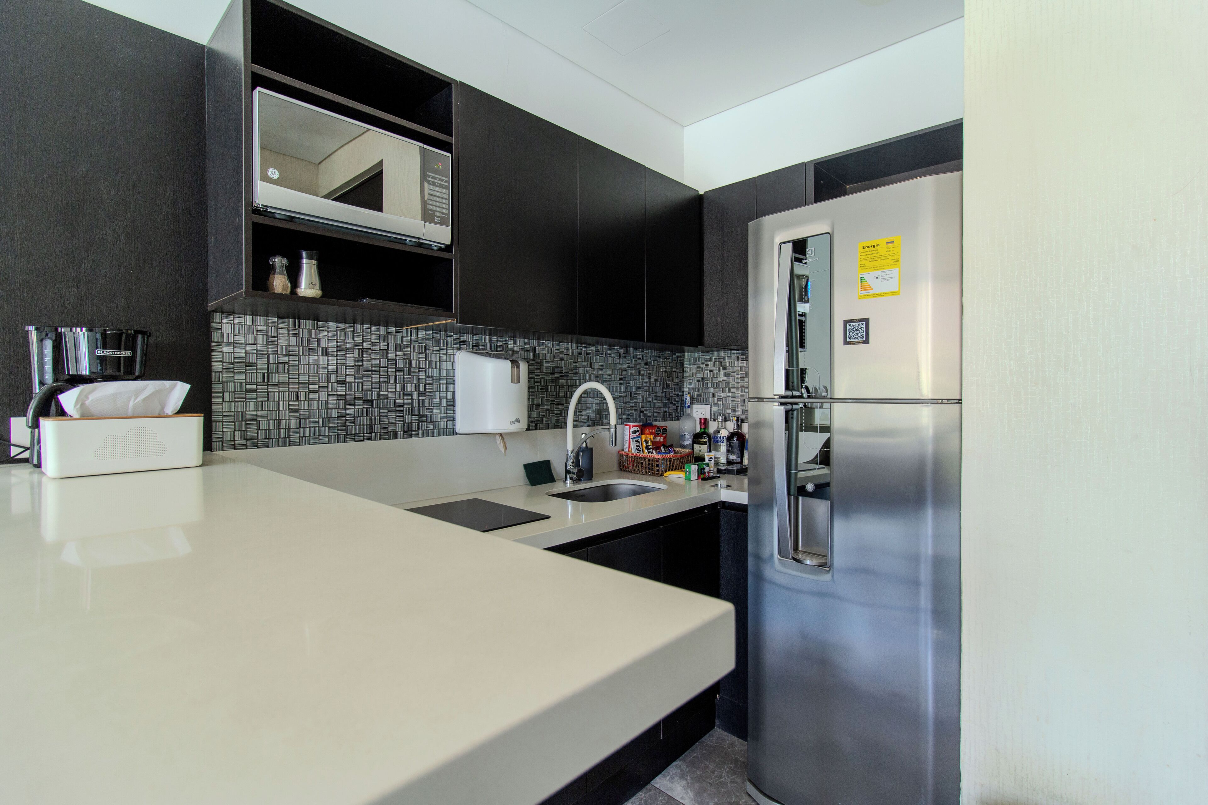 Une cuisine moderne avec des meubles de couleur sombre, un réfrigérateur en acier inoxydable, un four à micro-ondes et un revêtement mural en carreaux.