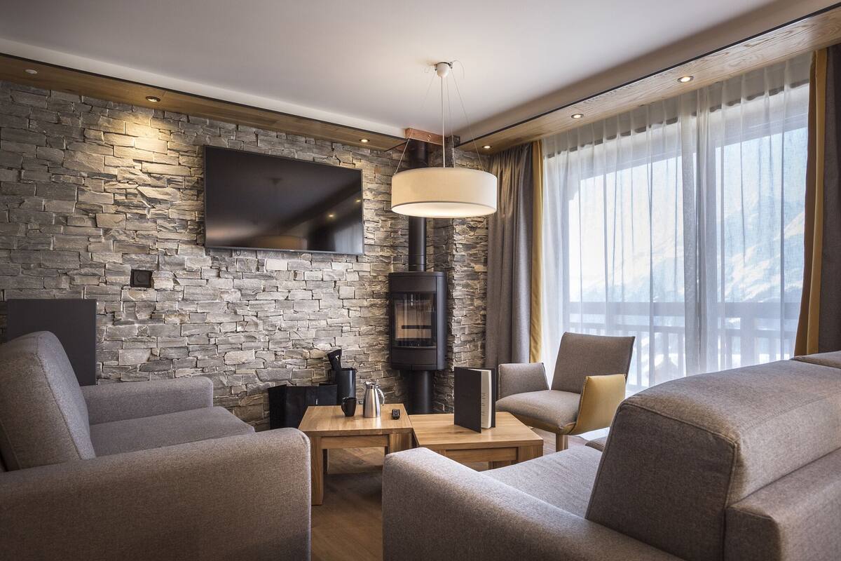 A modern living room with a stone wall, a flat-screen TV, a fireplace, and comfortable seating.