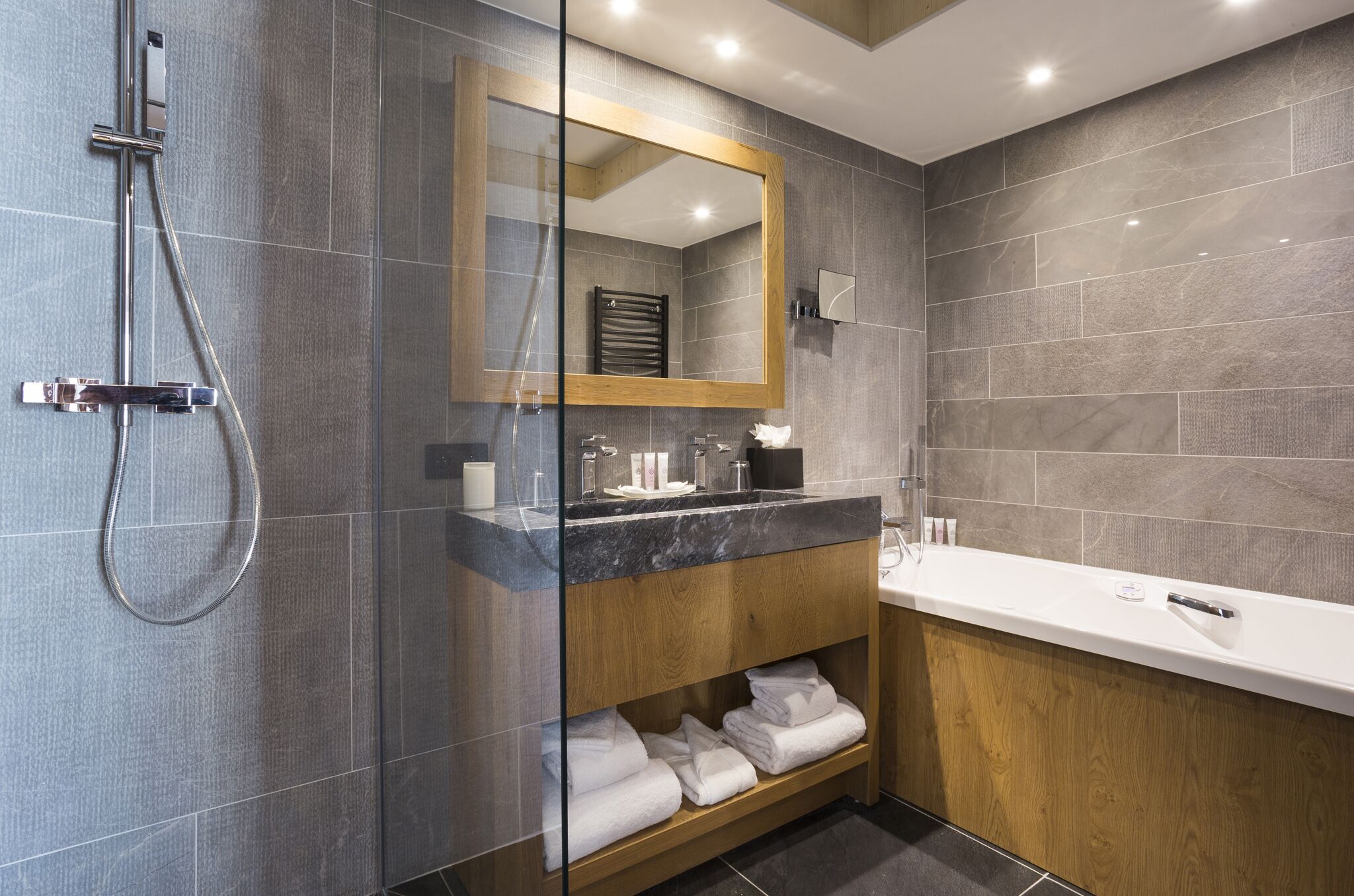 Une salle de bain moderne dotée d’une douche à parois de verre, d’un meuble-lavabo en bois avec un plan de toilette en marbre et d’un grand miroir.