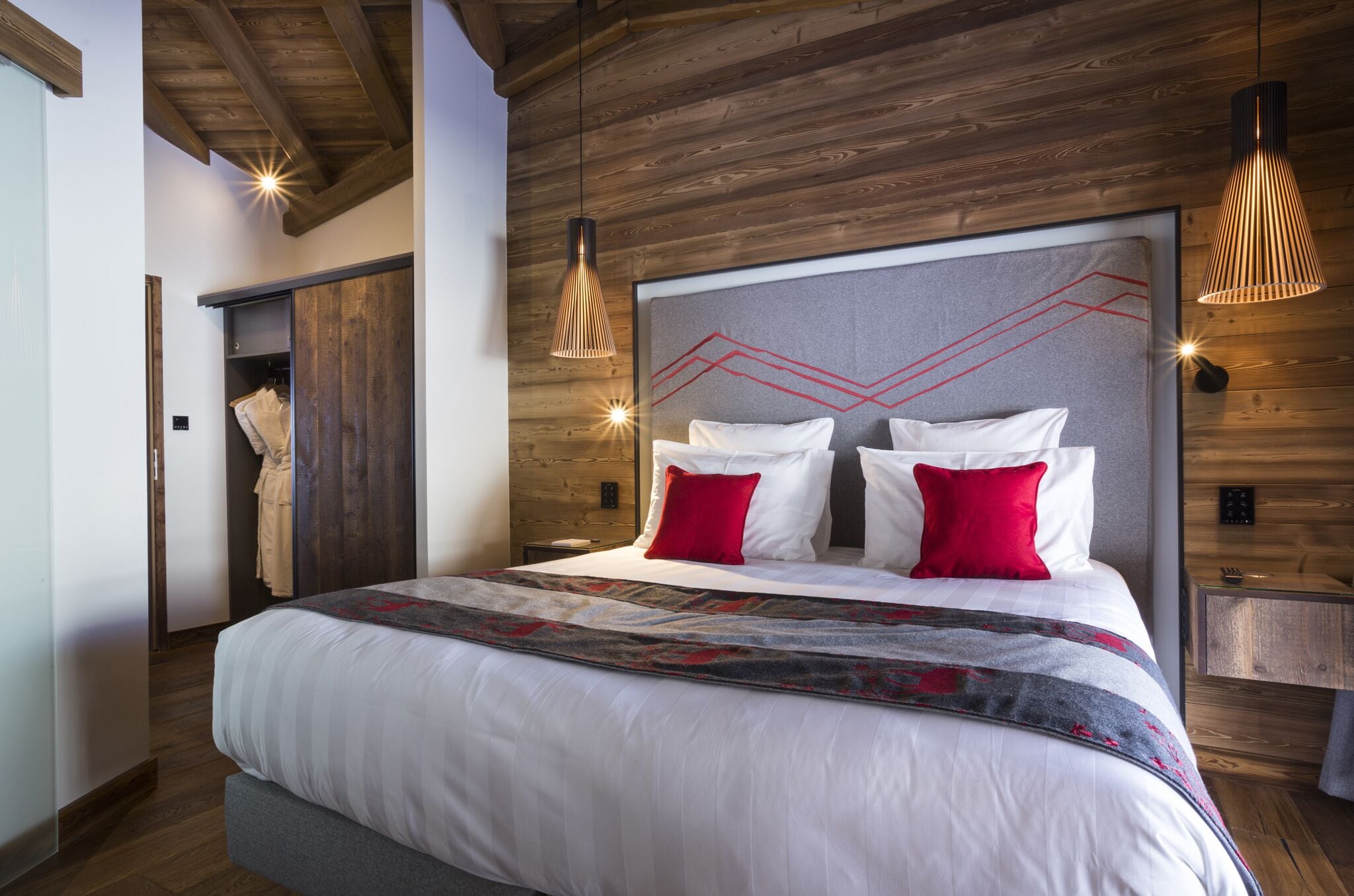 Een moderne slaapkamer met een groot bed, houten balken in het plafond en een hoofdbord met een geometrisch ontwerp.