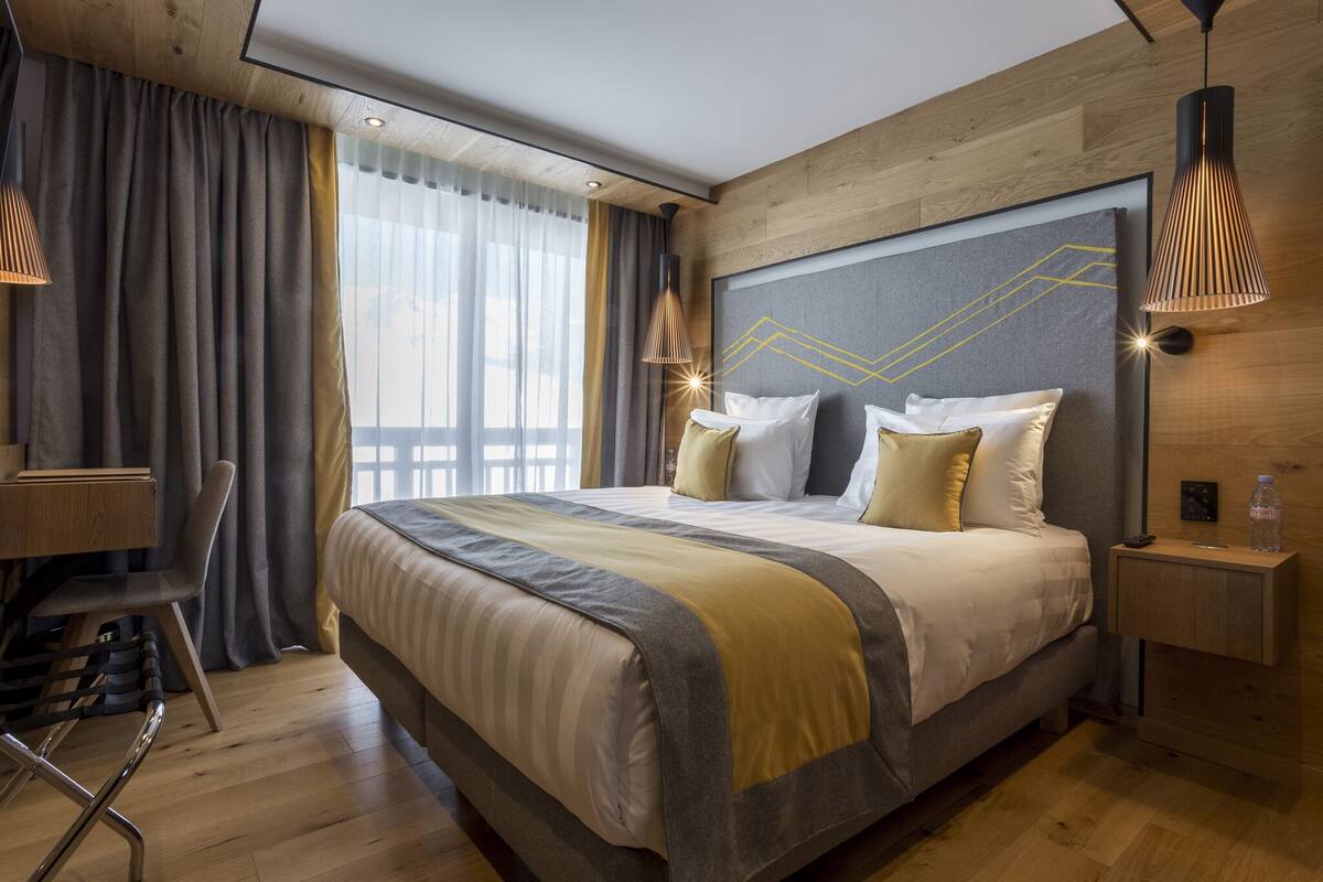 A modern hotel room with a large bed, a desk, and a chair.