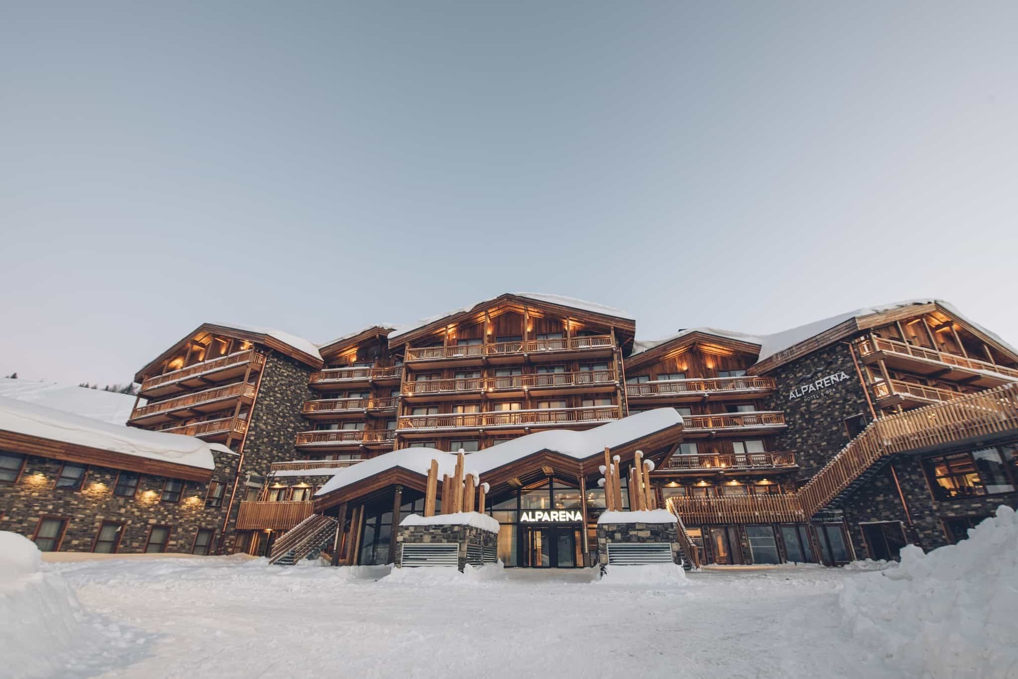 A multi-story hotel with a stone facade, wooden balconies, and a sign reading "ALPARENA HOTEL."