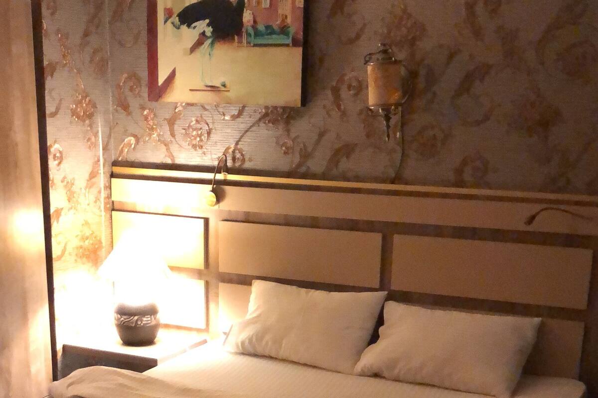 A hotel room with a bed, a nightstand, a lamp, and a painting on the wall.